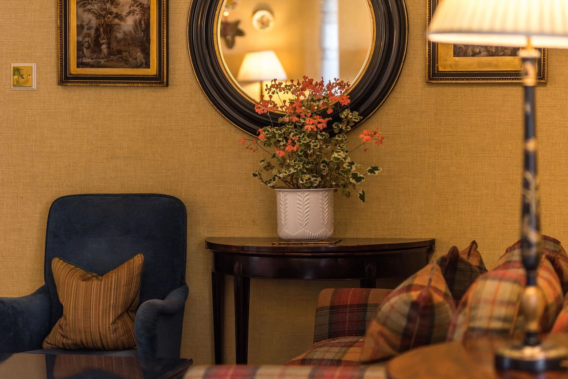 A corner of a Greywalls sitting room: a round mirror, geraniums and tartan cushions