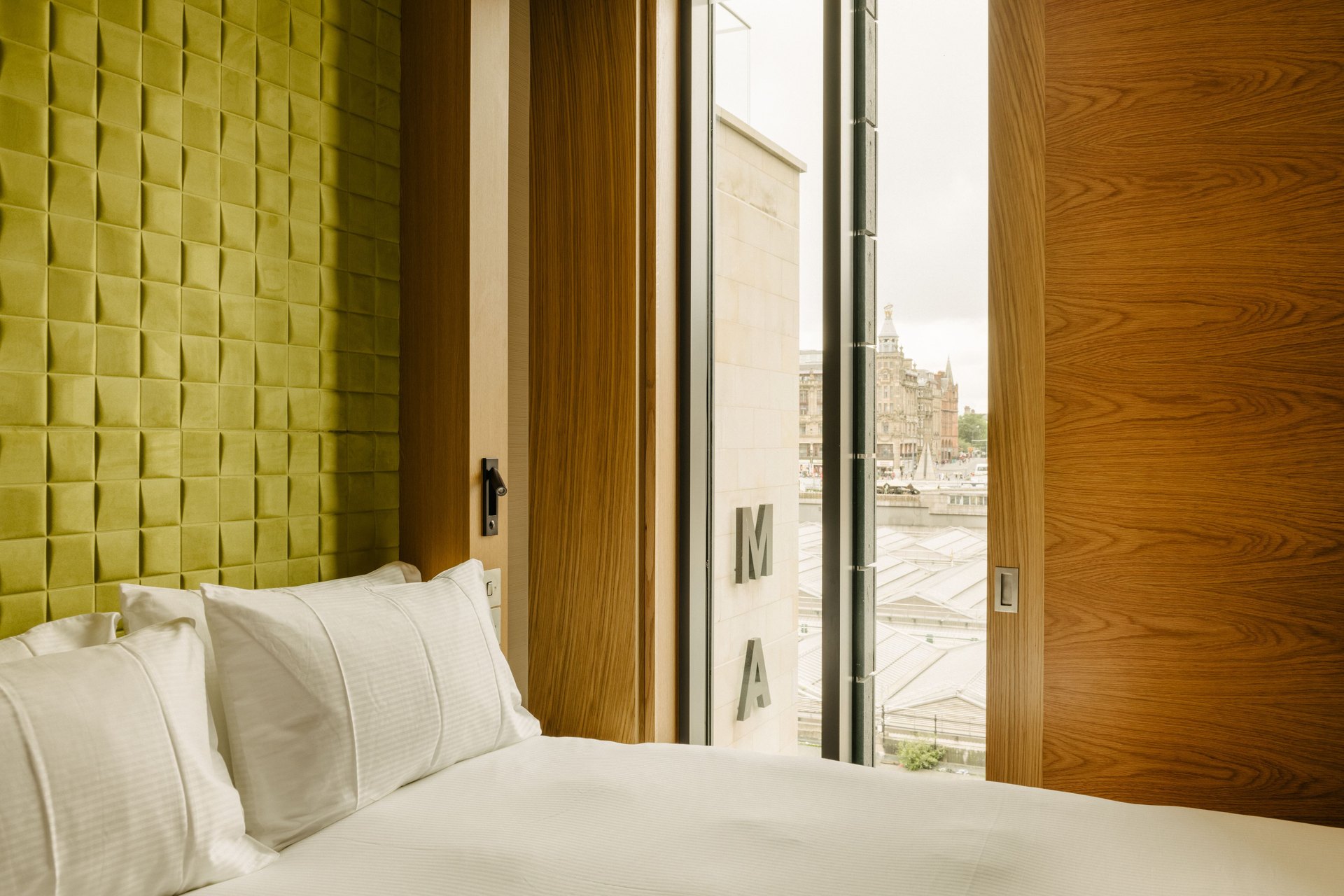 A bedroom at Market Street Hotel, oak panels open on the roofs of Waverley station