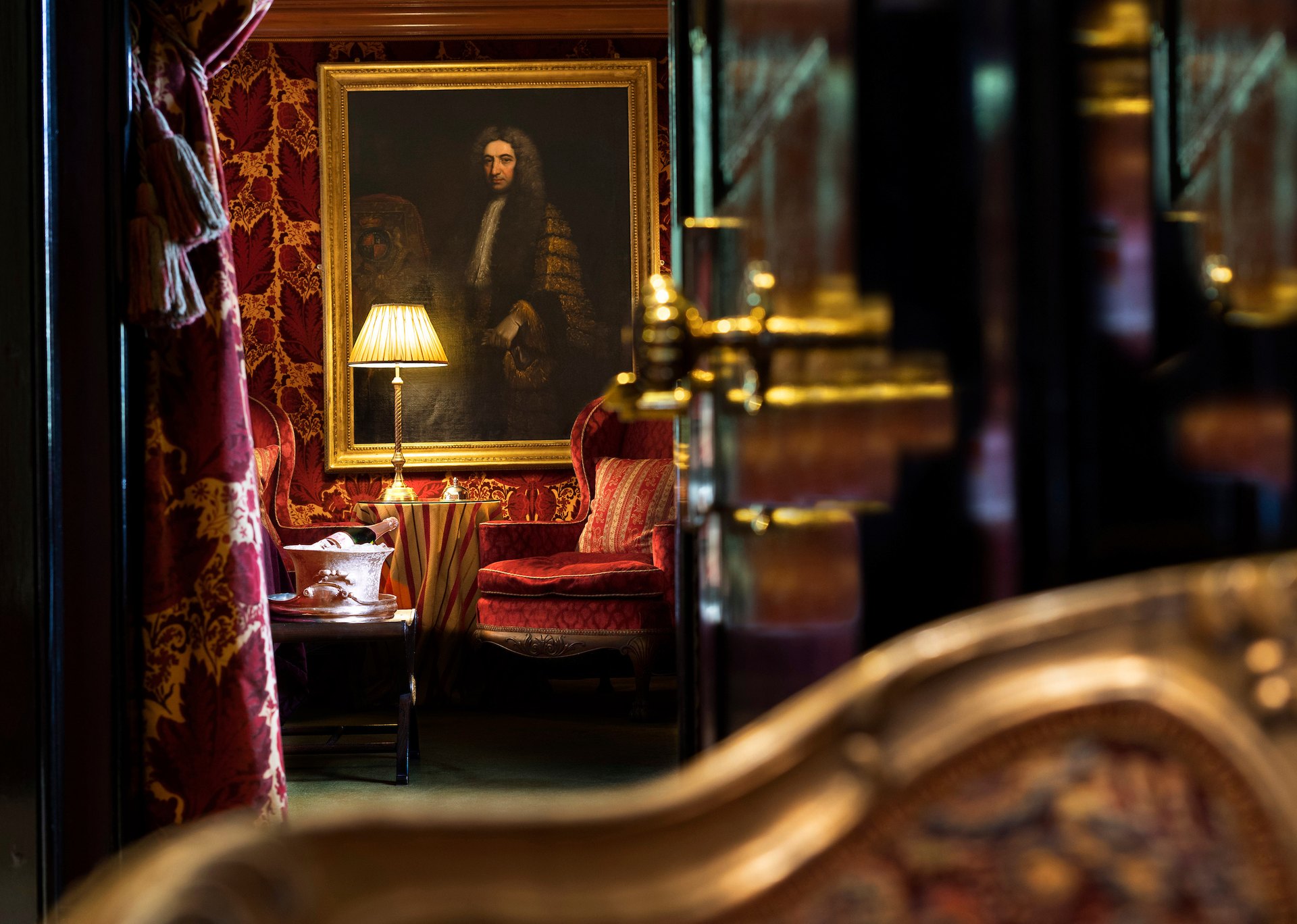 A red damask sitting room at Prestonfield, a portrait in a gilt frame above the armchairs