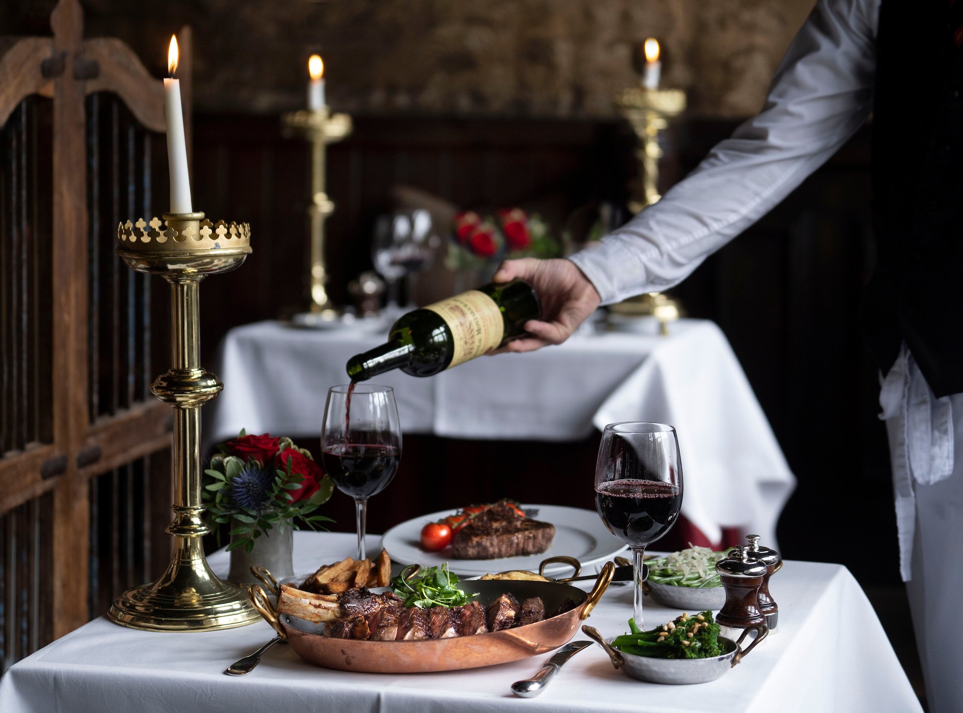 Red wine poured beside a steak in a copper pan, by candlelight in the Witchery dining room
